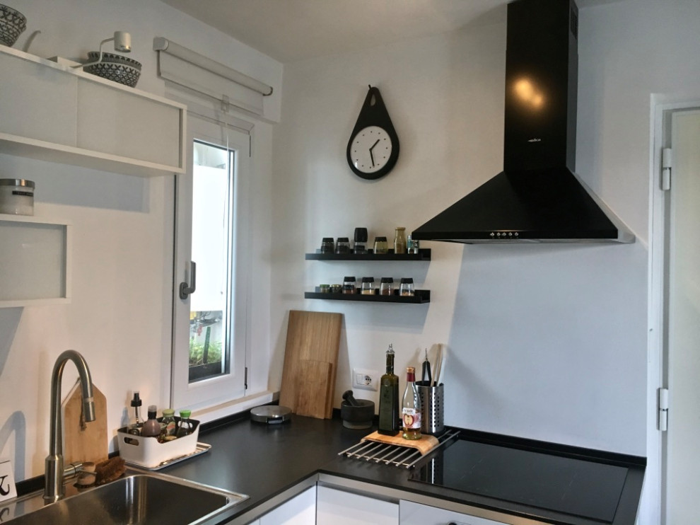 Immagine di una piccola cucina scandinava con lavello da incasso, ante bianche, top in laminato, elettrodomestici bianchi, pavimento in cemento, nessuna isola, pavimento grigio e top nero