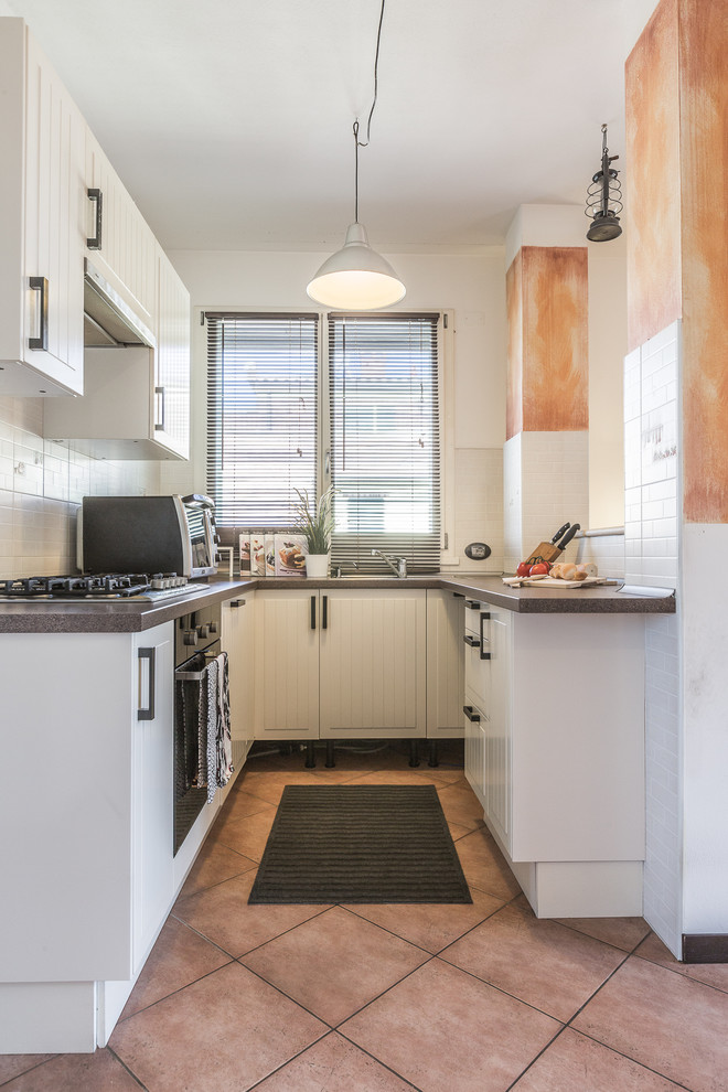 ボローニャにあるトランジショナルスタイルのおしゃれなコの字型キッチン (白いキャビネット、白いキッチンパネル、黒い調理設備、御影石カウンター、セラミックタイルのキッチンパネル、セラミックタイルの床) の写真