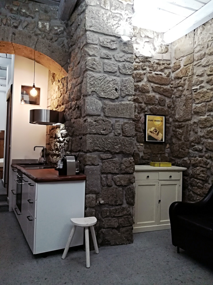 Immagine di una piccola cucina industriale con lavello a vasca singola, ante lisce, ante bianche, top in legno, elettrodomestici neri, pavimento in pietra calcarea e pavimento grigio