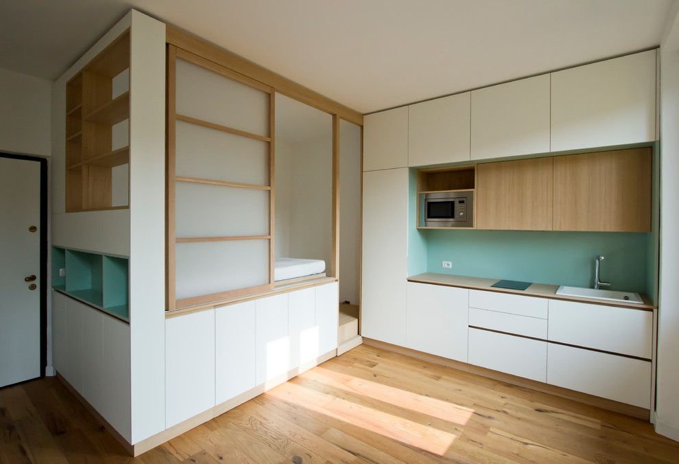 Photo of a small scandi single-wall open plan kitchen in Milan with light hardwood flooring, a built-in sink, flat-panel cabinets, white cabinets, green splashback, stainless steel appliances, no island and beige worktops.