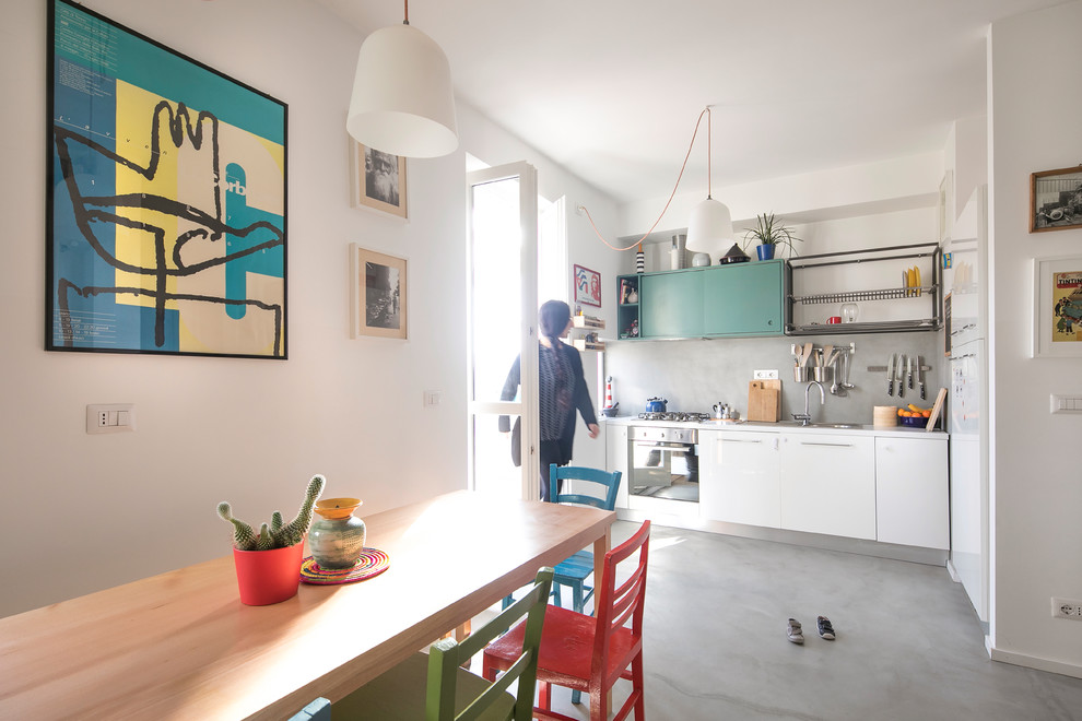 На фото: кухня в стиле фьюжн с обеденным столом, плоскими фасадами, белыми фасадами, серым фартуком, бетонным полом и серым полом
