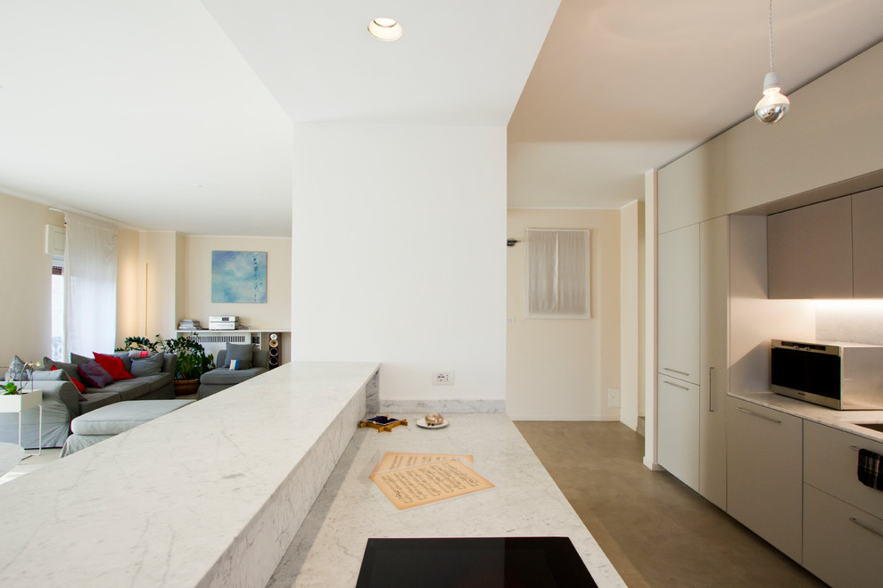 Modern inredning av ett stort vit vitt kök, med en undermonterad diskho, släta luckor, grå skåp, marmorbänkskiva, vitt stänkskydd, stänkskydd i marmor, svarta vitvaror, betonggolv, en köksö och grått golv