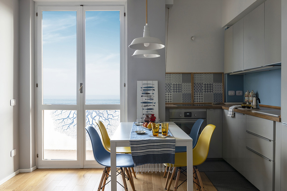 Small contemporary l-shaped kitchen/diner in Milan with a built-in sink, flat-panel cabinets, grey cabinets, laminate countertops, blue splashback, metal splashback, integrated appliances, light hardwood flooring, no island, beige floors and brown worktops.