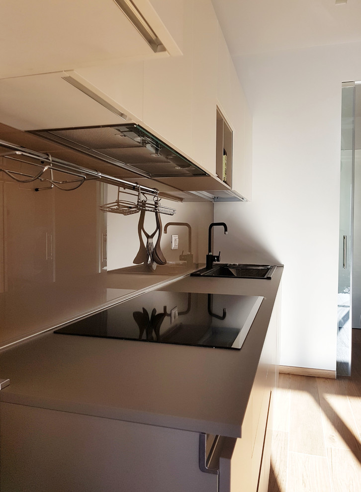 Design ideas for a large contemporary galley open plan kitchen in Milan with a single-bowl sink, flat-panel cabinets, beige cabinets, composite countertops, beige splashback, glass sheet splashback, black appliances, porcelain flooring, a breakfast bar, brown floors and beige worktops.