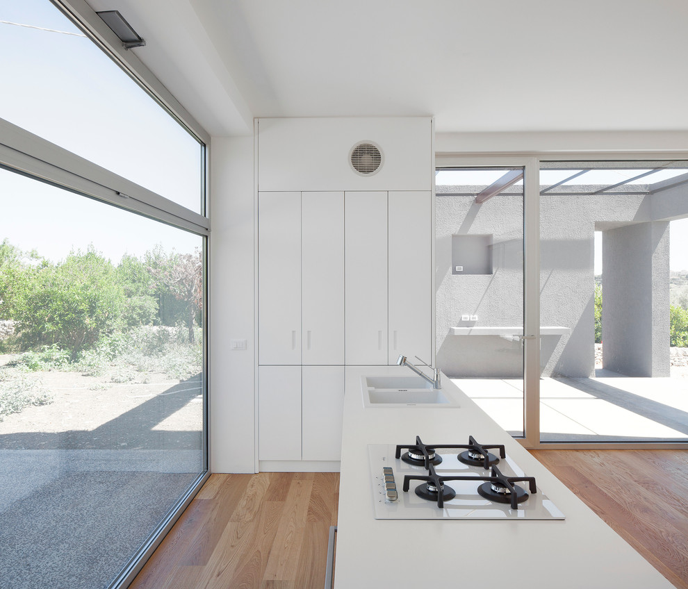 Immagine di una grande cucina minimal con lavello da incasso, ante lisce, ante bianche, parquet chiaro e penisola