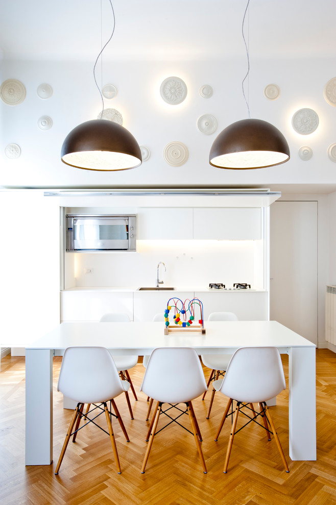 Photo of a contemporary single-wall kitchen/diner in Milan with a built-in sink, flat-panel cabinets, white cabinets, white splashback, stainless steel appliances and medium hardwood flooring.