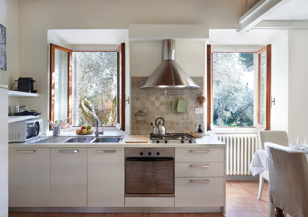 Modelo de cocina comedor lineal de estilo de casa de campo de tamaño medio sin isla con armarios con paneles lisos, salpicadero de azulejos de cerámica, electrodomésticos de acero inoxidable, suelo de baldosas de terracota, encimeras blancas, fregadero de doble seno, puertas de armario de madera clara, salpicadero marrón y suelo marrón