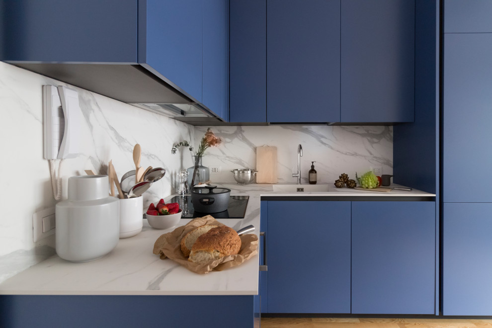 Small contemporary l-shaped kitchen in Milan with an integrated sink, flat-panel cabinets, blue cabinets, grey splashback, integrated appliances, beige floors and grey worktops.
