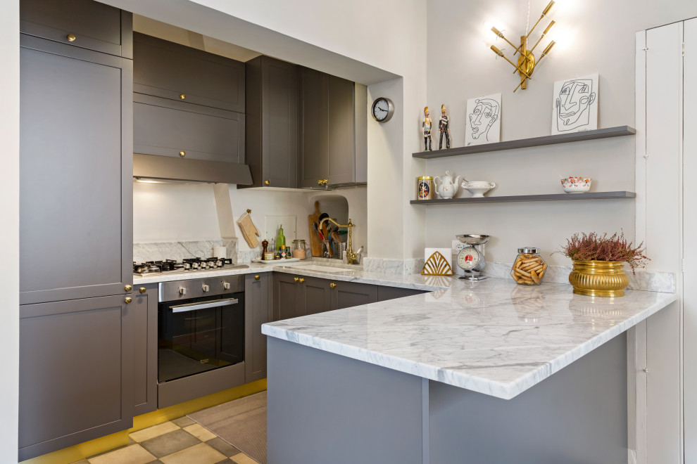 Inredning av ett klassiskt litet grå grått kök, med en undermonterad diskho, grå skåp, rostfria vitvaror, en halv köksö, grått golv, luckor med infälld panel, marmorbänkskiva, grått stänkskydd, stänkskydd i marmor och cementgolv
