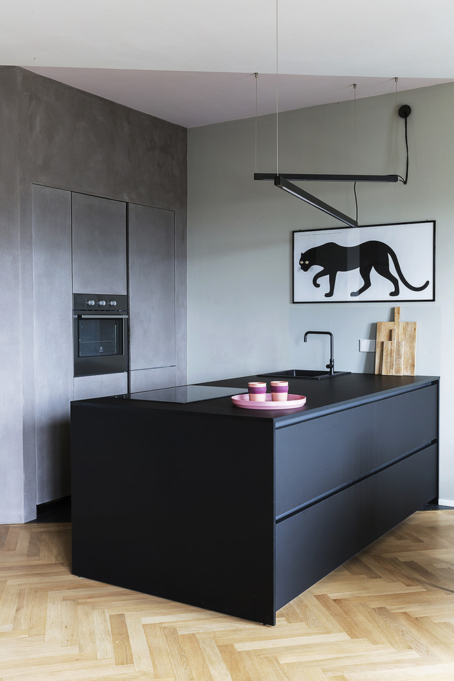 Zweizeilige Moderne Küche mit schwarzen Schränken, Küchengeräten aus Edelstahl, schwarzer Arbeitsplatte, Einbauwaschbecken, flächenbündigen Schrankfronten, hellem Holzboden, Halbinsel und braunem Boden in Turin