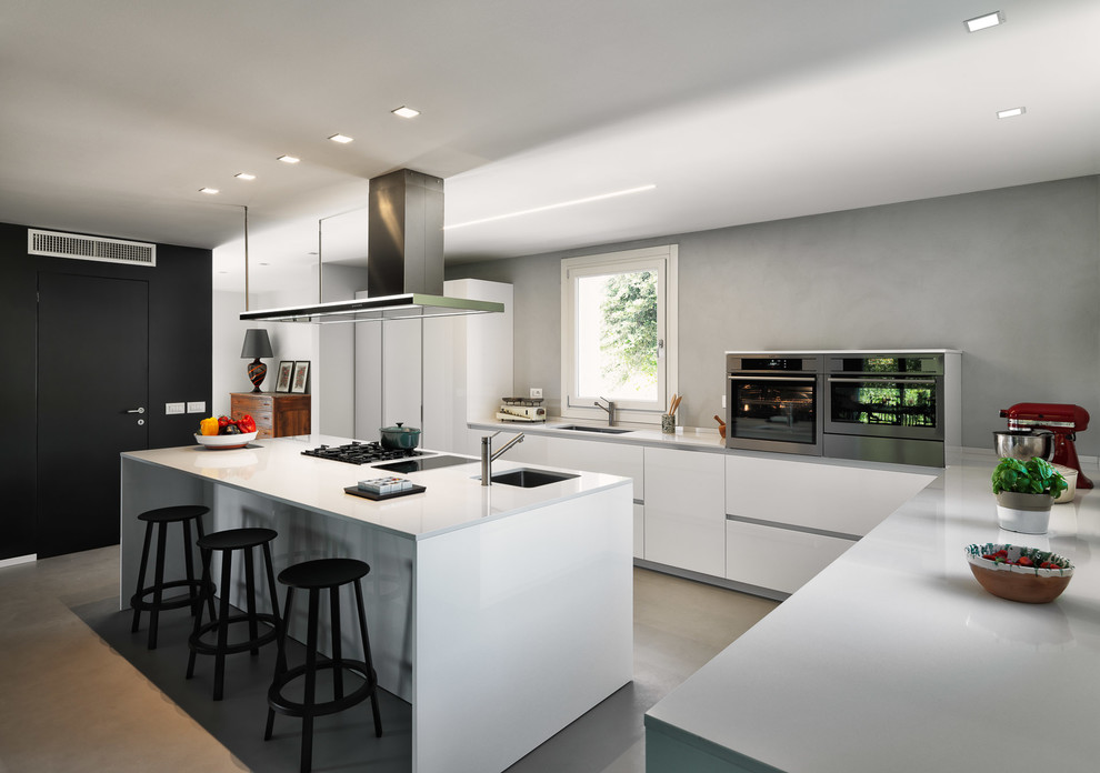 Idéer för att renovera ett funkis vit vitt l-kök, med släta luckor, vita skåp, rostfria vitvaror, en köksö, en undermonterad diskho, grått stänkskydd, betonggolv och grått golv