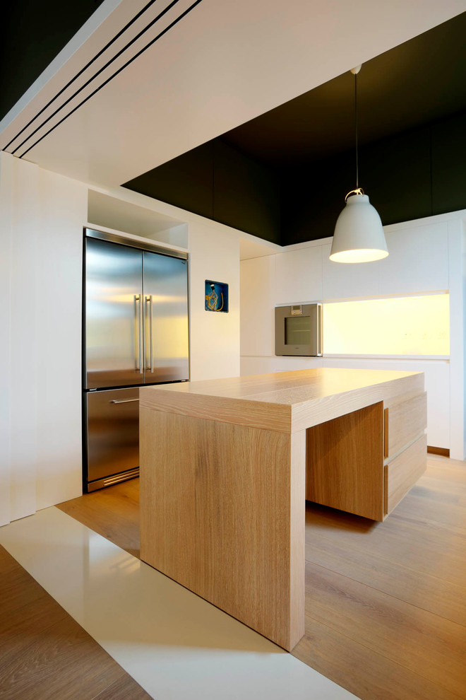 На фото: прямая кухня в стиле модернизм с обеденным столом, техникой из нержавеющей стали, светлым паркетным полом, островом, плоскими фасадами, светлыми деревянными фасадами и деревянной столешницей с