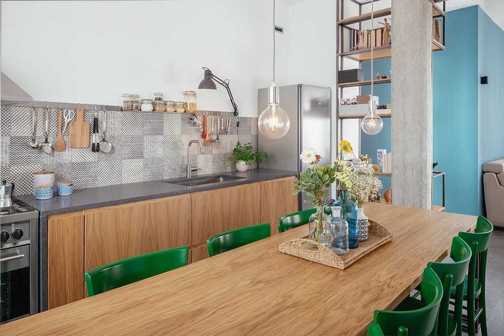 Пример оригинального дизайна: кухня в стиле лофт с обеденным столом, полом из керамогранита, серым полом, врезной мойкой, плоскими фасадами, светлыми деревянными фасадами, разноцветным фартуком и серой столешницей