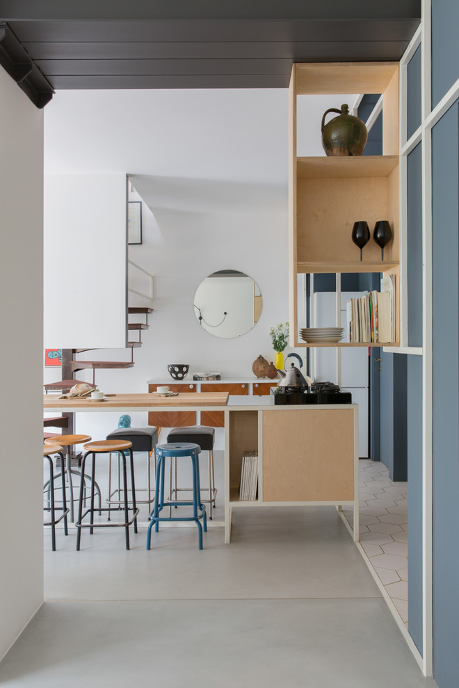 Inspiration pour une cuisine ouverte linéaire design en bois clair avec un placard sans porte, un électroménager noir, sol en béton ciré et un sol gris.