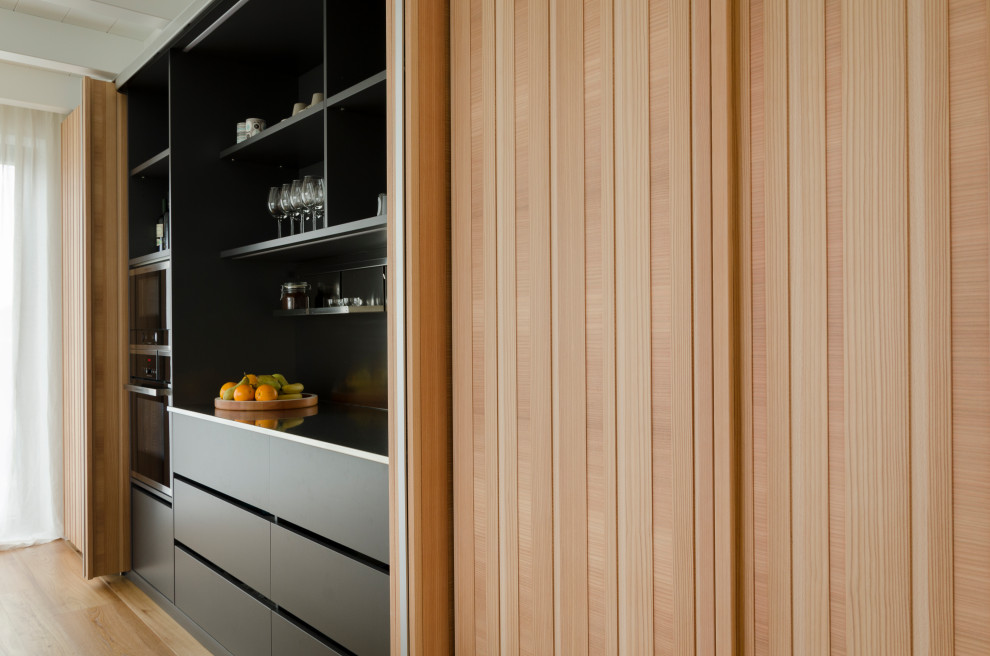 Immagine di una cucina scandinava di medie dimensioni con lavello integrato, ante lisce, ante bianche, top in superficie solida, elettrodomestici neri, parquet chiaro, top bianco e travi a vista