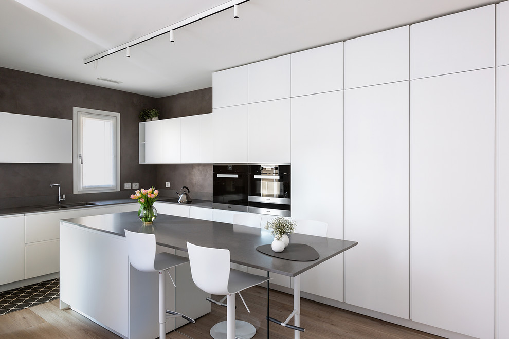 Modern inredning av ett mellanstort grå grått l-kök, med en dubbel diskho, släta luckor, vita skåp, bänkskiva i kvarts, svarta vitvaror, en köksö, mellanmörkt trägolv och brunt golv
