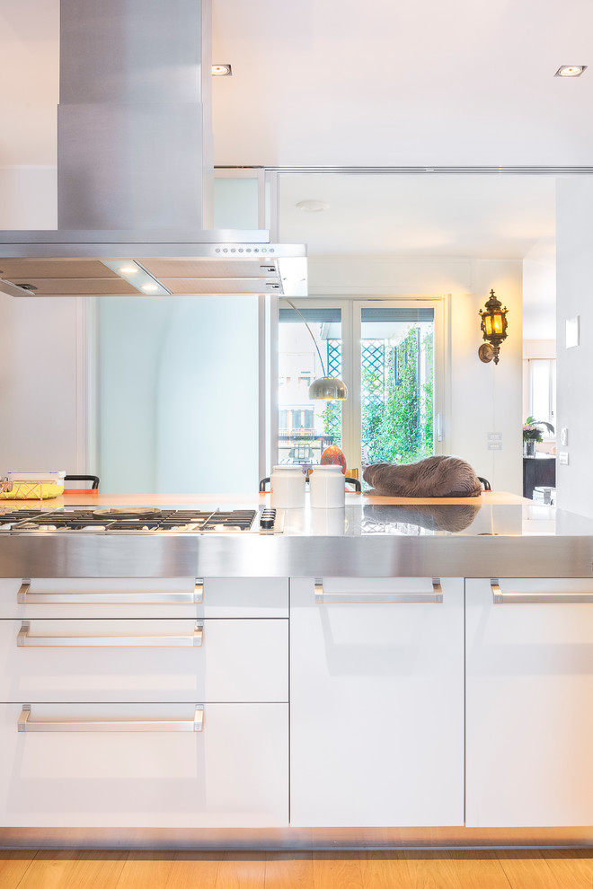 Idéer för att renovera ett mellanstort medelhavsstil kök, med en nedsänkt diskho, släta luckor, vita skåp, bänkskiva i rostfritt stål, rostfria vitvaror, målat trägolv och en köksö