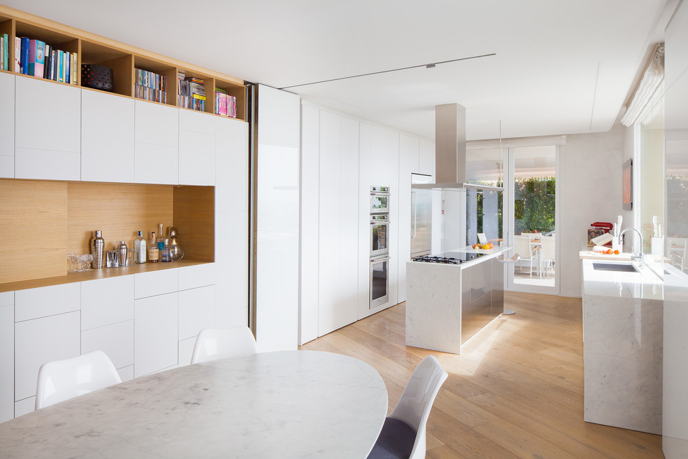 Idéer för ett modernt kök och matrum, med släta luckor, vita skåp, marmorbänkskiva, rostfria vitvaror, en köksö, en undermonterad diskho och ljust trägolv