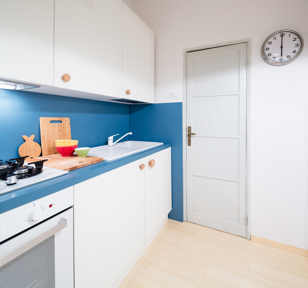 Bild på ett litet funkis linjärt kök med öppen planlösning, med en nedsänkt diskho, släta luckor, vita skåp, laminatbänkskiva, blått stänkskydd, vita vitvaror, bambugolv, glaspanel som stänkskydd och brunt golv