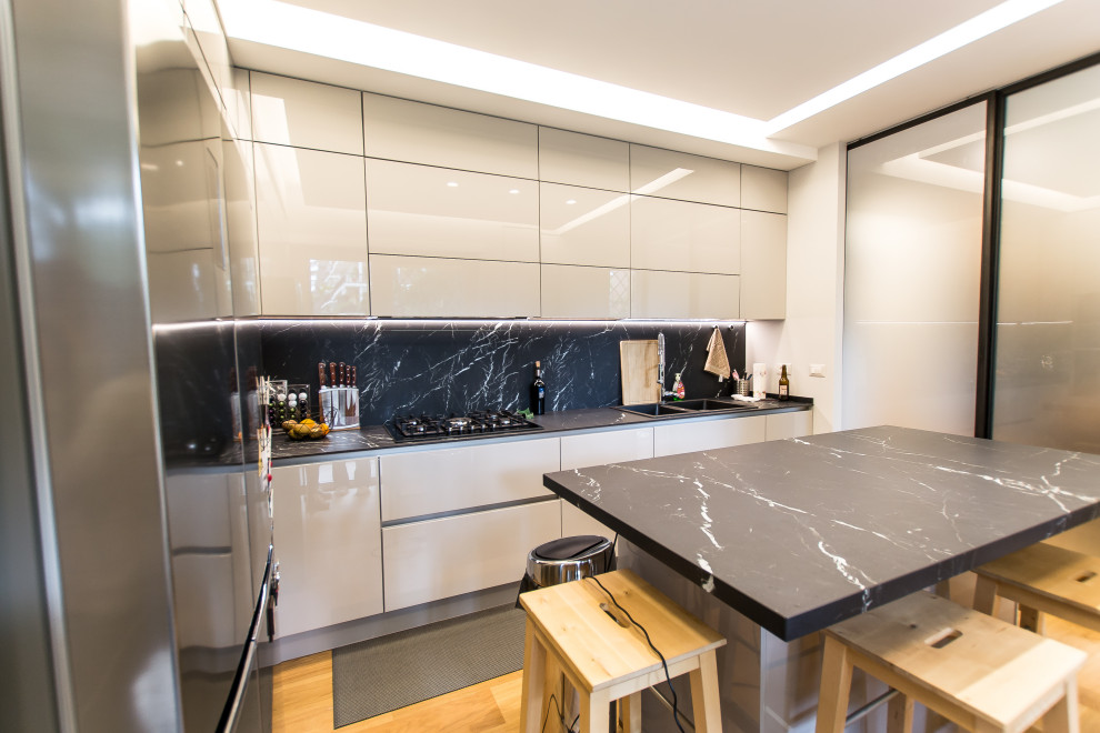 Inredning av ett modernt svart svart kök med öppen planlösning, med en dubbel diskho, luckor med profilerade fronter, grå skåp, marmorbänkskiva, svart stänkskydd, stänkskydd i marmor, rostfria vitvaror, ljust trägolv och en köksö