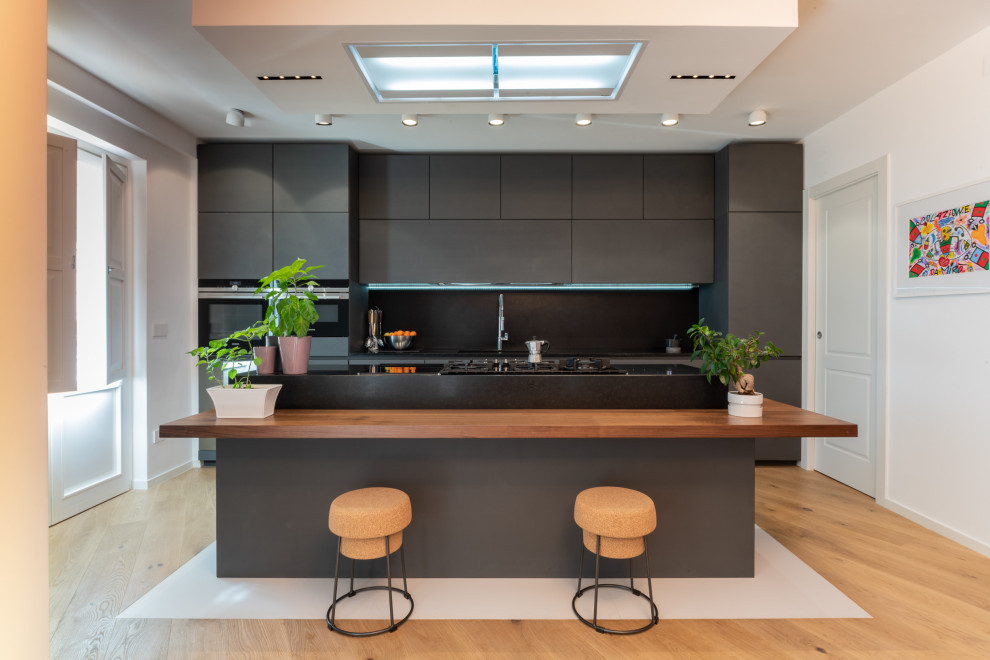 Идея дизайна: параллельная кухня в современном стиле с плоскими фасадами, серыми фасадами, черным фартуком, черной техникой, паркетным полом среднего тона, островом и коричневым полом