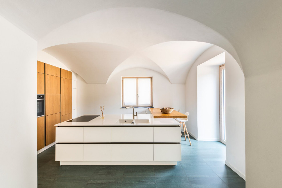 Modelo de cocina abovedada mediterránea con fregadero integrado, armarios con paneles lisos, puertas de armario de madera oscura, una isla y encimeras blancas