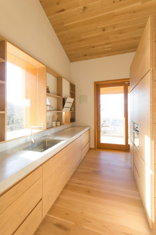Immagine di una cucina parallela nordica con lavello sottopiano, ante lisce, ante in legno chiaro, parquet chiaro e nessuna isola