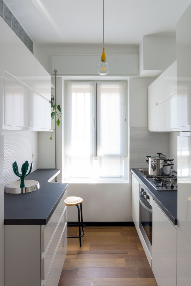 Photo of a small contemporary galley enclosed kitchen in Rome with a single-bowl sink, beaded cabinets, white cabinets, engineered stone countertops, white splashback, mosaic tiled splashback, stainless steel appliances, porcelain flooring, no island, brown floors and grey worktops.