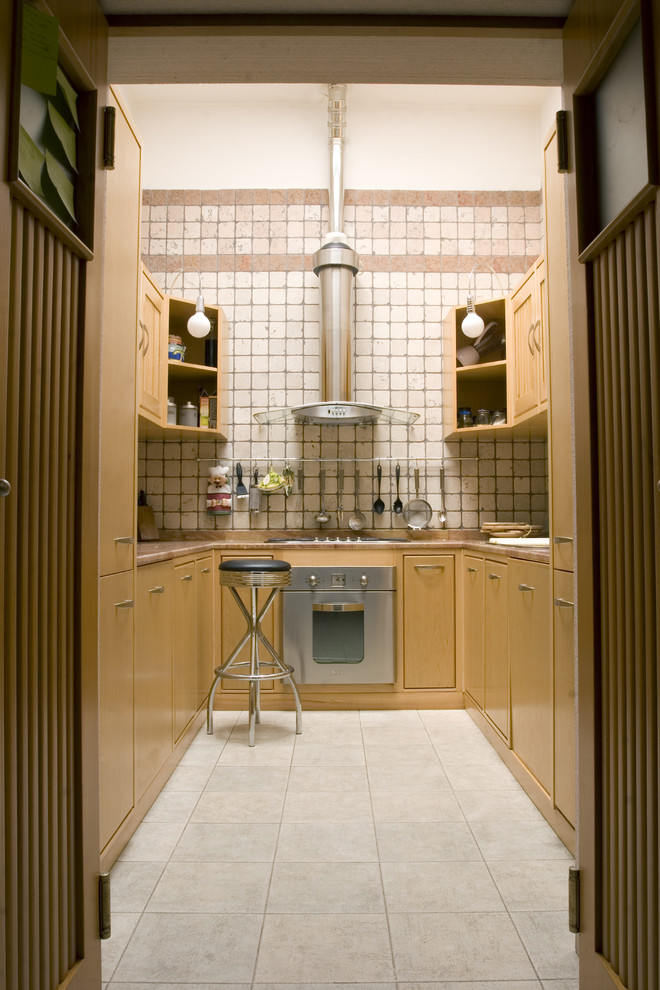 バーリにあるカントリー風のおしゃれなコの字型キッチン (淡色木目調キャビネット、ベージュキッチンパネル、シルバーの調理設備) の写真