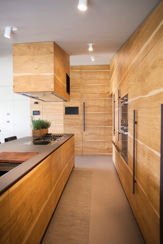Foto på ett funkis l-kök, med släta luckor, skåp i ljust trä, svart stänkskydd, integrerade vitvaror, en köksö och beiget golv