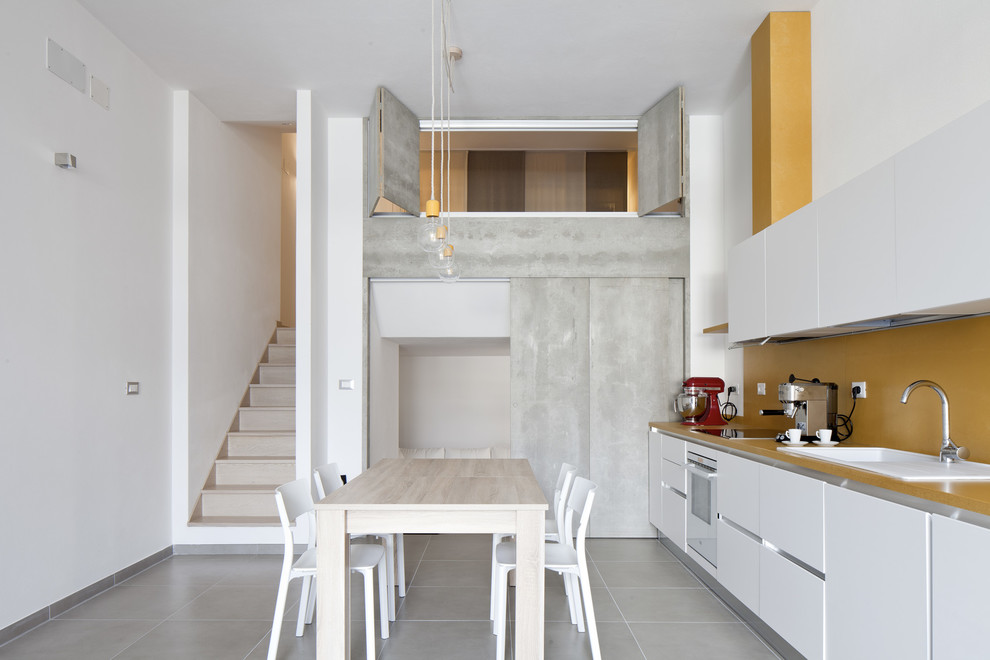 Foto di una cucina design di medie dimensioni con ante lisce, ante bianche, paraspruzzi giallo, nessuna isola, pavimento grigio, lavello da incasso e elettrodomestici bianchi