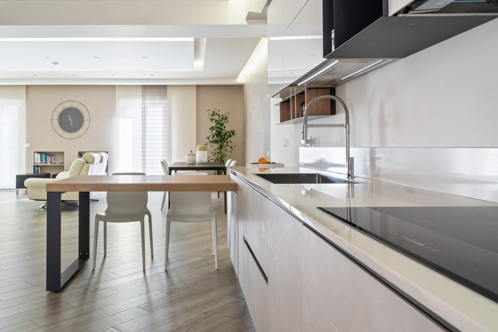 Idéer för att renovera ett mellanstort funkis vit linjärt vitt kök med öppen planlösning, med en nedsänkt diskho, släta luckor, vita skåp, vitt stänkskydd, integrerade vitvaror, mellanmörkt trägolv, en halv köksö och beiget golv
