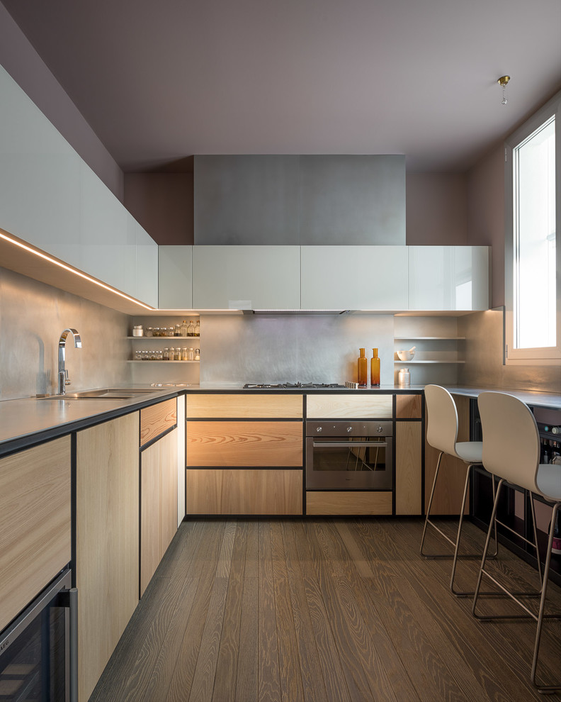 Foto di una cucina a L design con ante in legno chiaro, paraspruzzi grigio, lavello sottopiano, ante lisce, elettrodomestici in acciaio inossidabile, pavimento in legno massello medio, pavimento marrone e top grigio