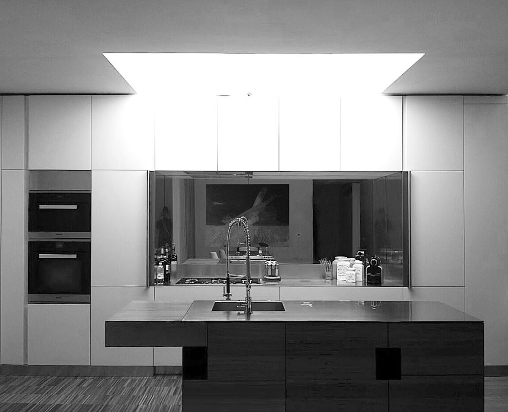 Exempel på ett mellanstort modernt grå linjärt grått kök med öppen planlösning, med en undermonterad diskho, släta luckor, skåp i ljust trä, bänkskiva i rostfritt stål, grått stänkskydd, spegel som stänkskydd, rostfria vitvaror, målat trägolv, en köksö och brunt golv