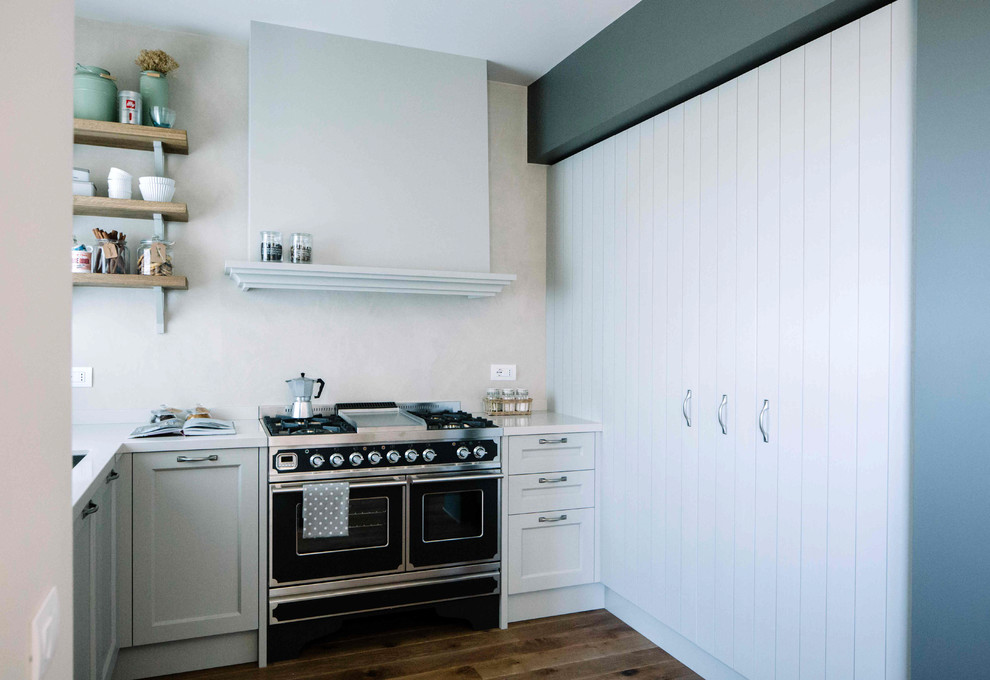 Klassische Küche ohne Insel in L-Form mit Schrankfronten mit vertiefter Füllung, grauen Schränken, Küchenrückwand in Grau, schwarzen Elektrogeräten und braunem Holzboden in Sonstige