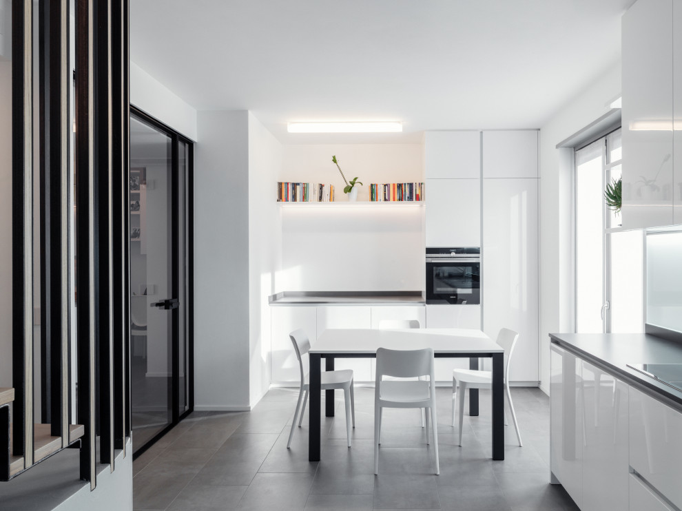 Moderne Wohnküche ohne Insel in L-Form mit flächenbündigen Schrankfronten, weißen Schränken, Küchengeräten aus Edelstahl, grauem Boden und grauer Arbeitsplatte in Sonstige
