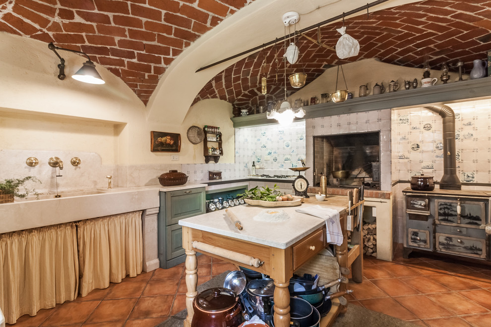 Example of a classic l-shaped terra-cotta tile and brown floor kitchen design in Other with an island, an integrated sink, white backsplash and white countertops