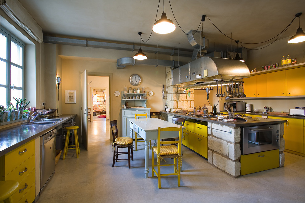 Bild på ett stort industriellt linjärt kök och matrum, med släta luckor, gula skåp, rostfria vitvaror, betonggolv, en halv köksö, en dubbel diskho och bänkskiva i rostfritt stål