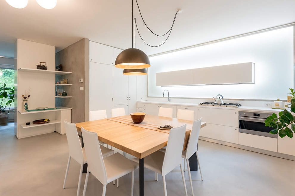 Moderne Wohnküche ohne Insel in L-Form mit flächenbündigen Schrankfronten, weißen Schränken, Küchenrückwand in Weiß, grauem Boden und weißer Arbeitsplatte in Sonstige