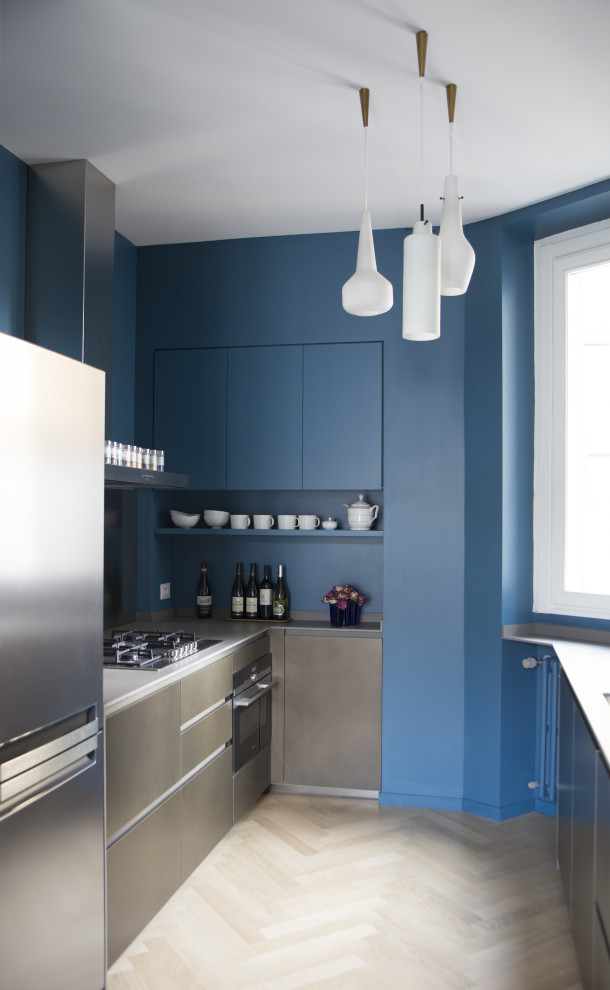На фото: угловая кухня среднего размера в современном стиле с плоскими фасадами, синими фасадами, синим фартуком, техникой из нержавеющей стали, бежевым полом и серой столешницей