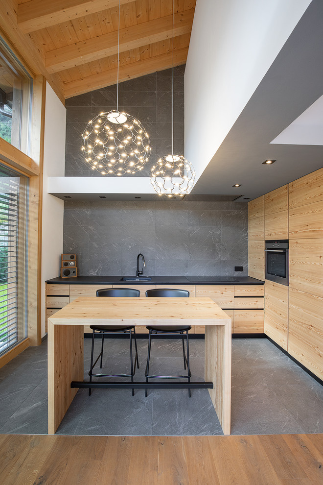 Immagine di un cucina con isola centrale minimal con lavello sottopiano, ante lisce, ante in legno scuro, paraspruzzi grigio, elettrodomestici da incasso, pavimento grigio e top nero