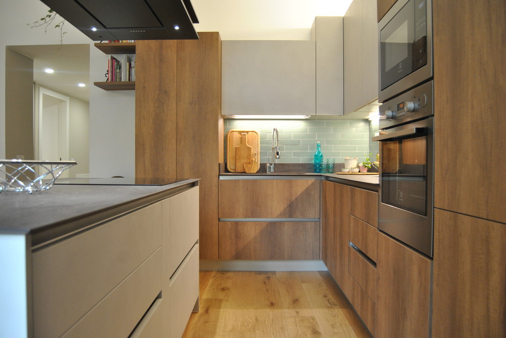 This is an example of a medium sized contemporary l-shaped kitchen/diner in Milan with an integrated sink, flat-panel cabinets, medium wood cabinets, composite countertops, matchstick tiled splashback, stainless steel appliances, light hardwood flooring, an island, brown floors and grey worktops.