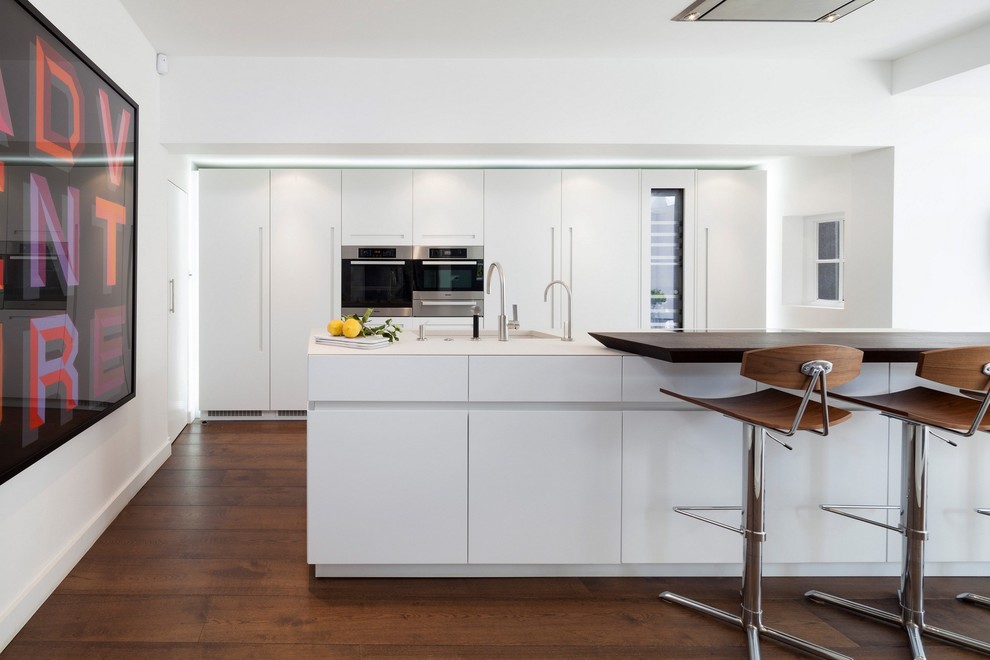Exempel på ett modernt kök, med släta luckor, vita skåp, rostfria vitvaror, mellanmörkt trägolv och en köksö