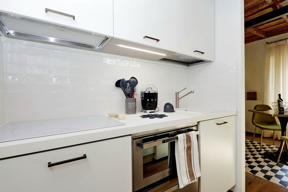 Small midcentury galley kitchen/diner in Rome with a built-in sink, flat-panel cabinets, white cabinets, laminate countertops, white splashback, ceramic splashback, white appliances, light hardwood flooring, no island and white worktops.