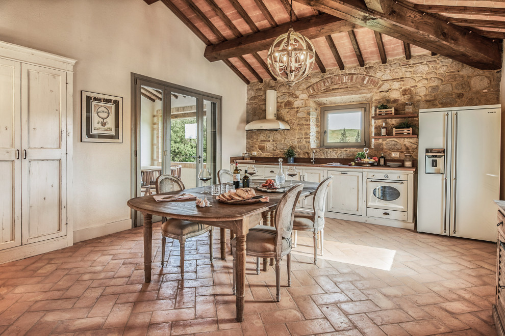 Mid-sized tuscan single-wall terra-cotta tile, brown floor and wood ceiling eat-in kitchen photo in Florence with an undermount sink, recessed-panel cabinets, white cabinets, brown backsplash, stone tile backsplash, white appliances, no island and brown countertops