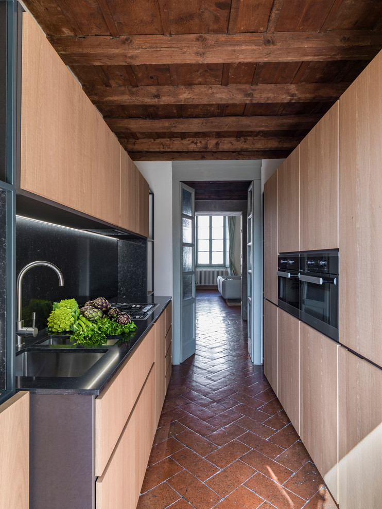 Idée de décoration pour une cuisine parallèle design en bois clair de taille moyenne avec un placard à porte plane, une crédence noire, tomettes au sol, aucun îlot, un évier encastré et un sol marron.