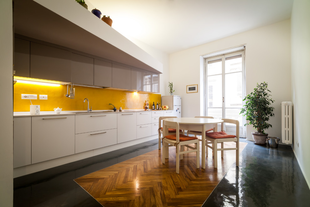 Пример оригинального дизайна: большая прямая кухня в современном стиле с обеденным столом, врезной мойкой, плоскими фасадами, белыми фасадами, желтым фартуком и полом из керамогранита