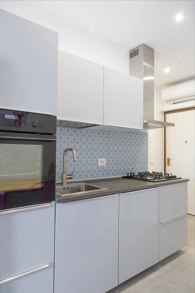 Foto di una piccola cucina lineare contemporanea con ante lisce, ante bianche, paraspruzzi blu, elettrodomestici neri e top grigio