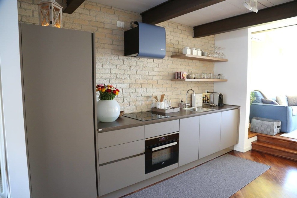 Foto på ett funkis linjärt kök, med en enkel diskho, släta luckor, grå skåp, stänkskydd i tegel, svarta vitvaror och mörkt trägolv