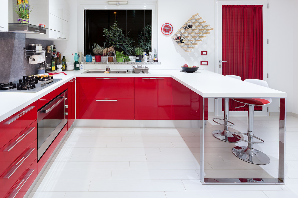 Moderne Küche in U-Form mit Doppelwaschbecken, flächenbündigen Schrankfronten, roten Schränken, Küchenrückwand in Grau, Küchengeräten aus Edelstahl und Halbinsel in Cagliari